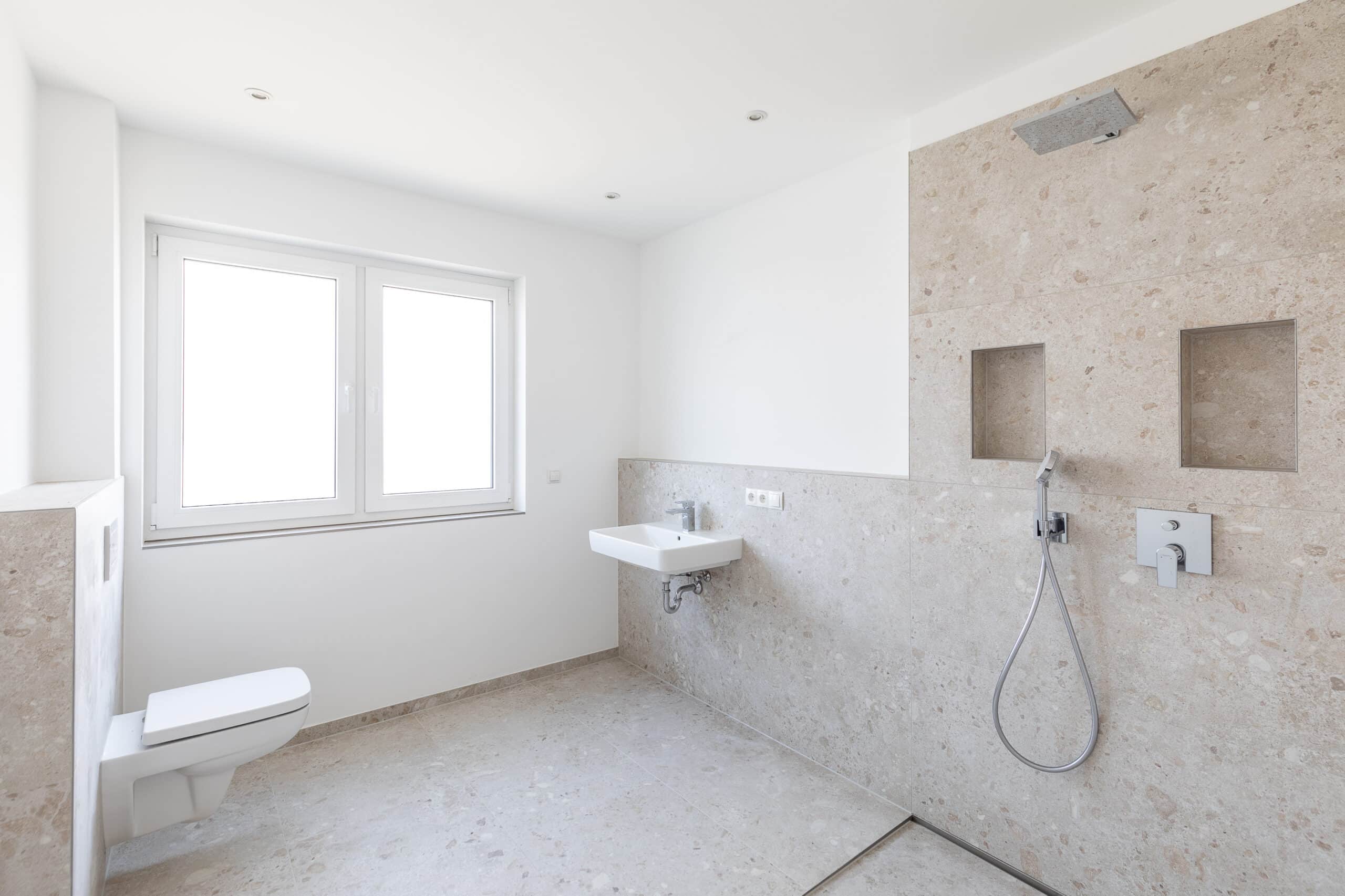 Helles Badezimmer mit Wandwaschbecken, WC und bodengleicher Dusche vor beigen Wandfliesen