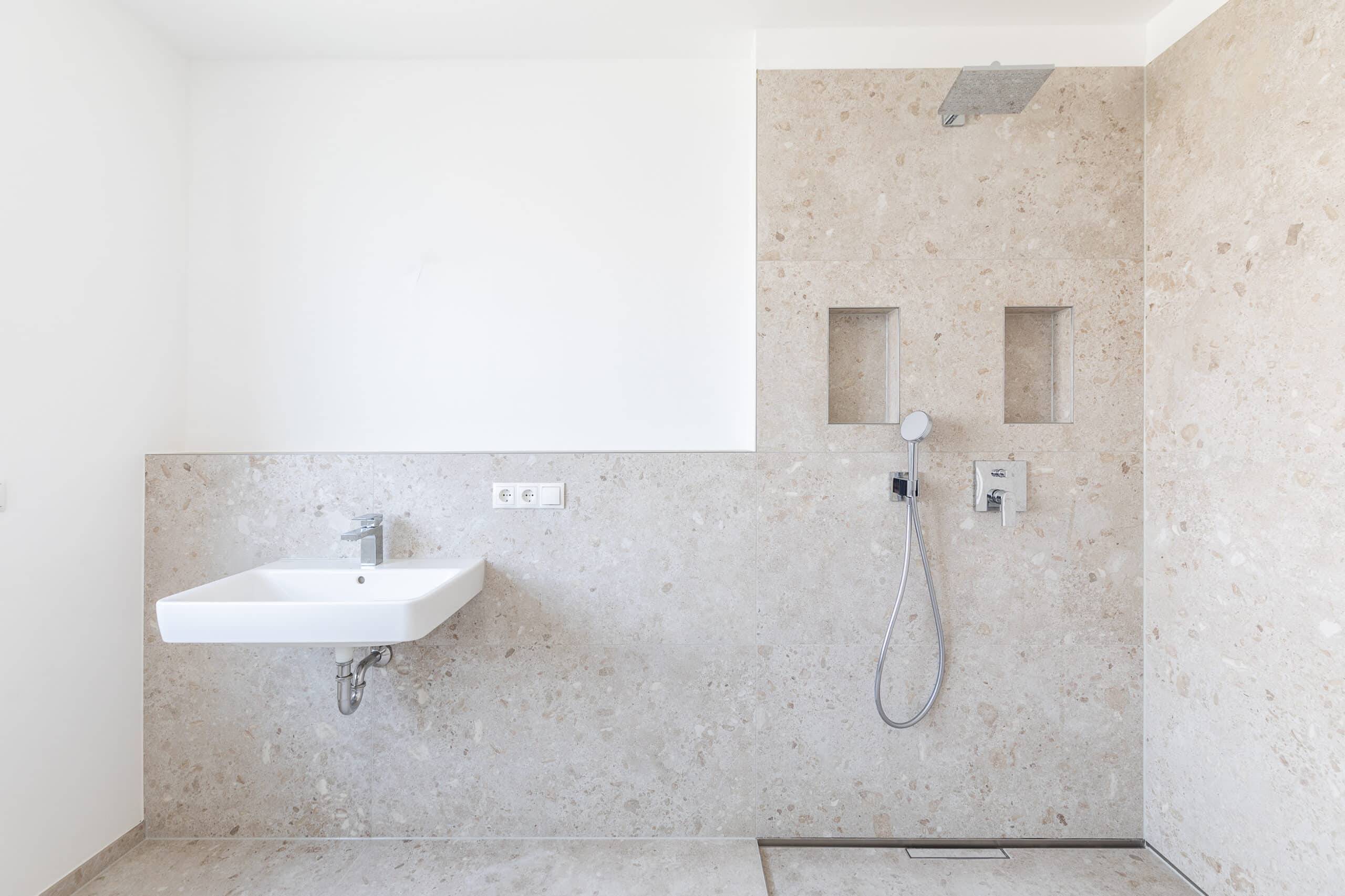 Wandwaschbecken neben einer bodengleichen Dusche mit Handbrause und Ablagenischen