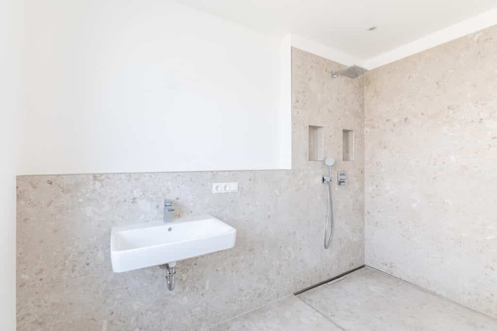 Bodengleiche Dusche mit Handbrause und Wandnischen neben einem Wandwaschbecken