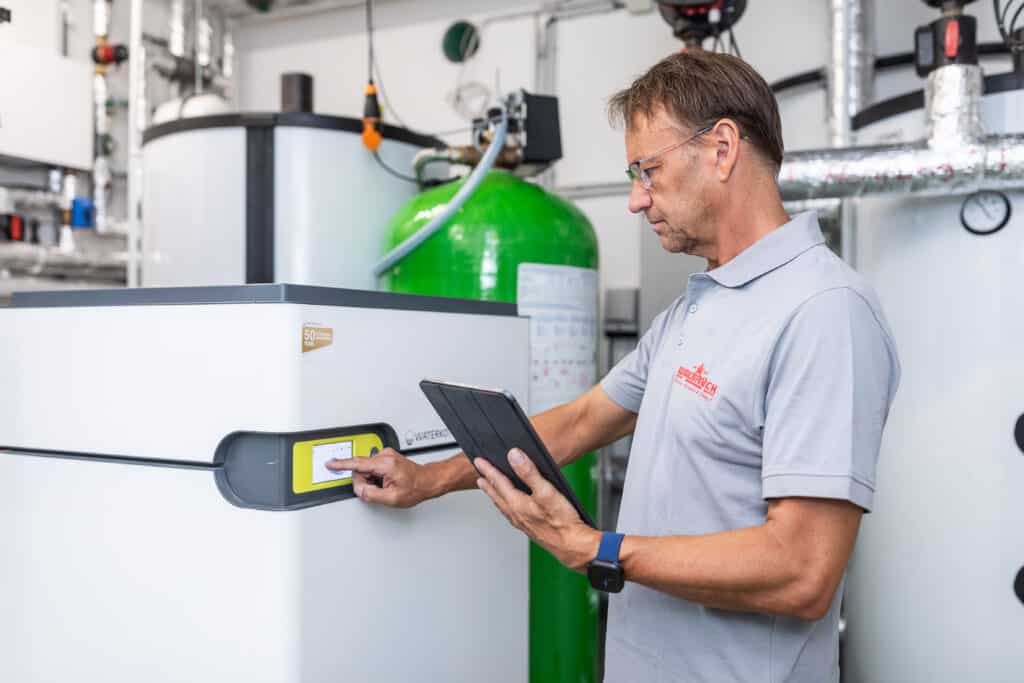 Walbrück-Techniker bedient die Wärmepumpenregelung und hält ein Tablet zur Anlagenprüfung