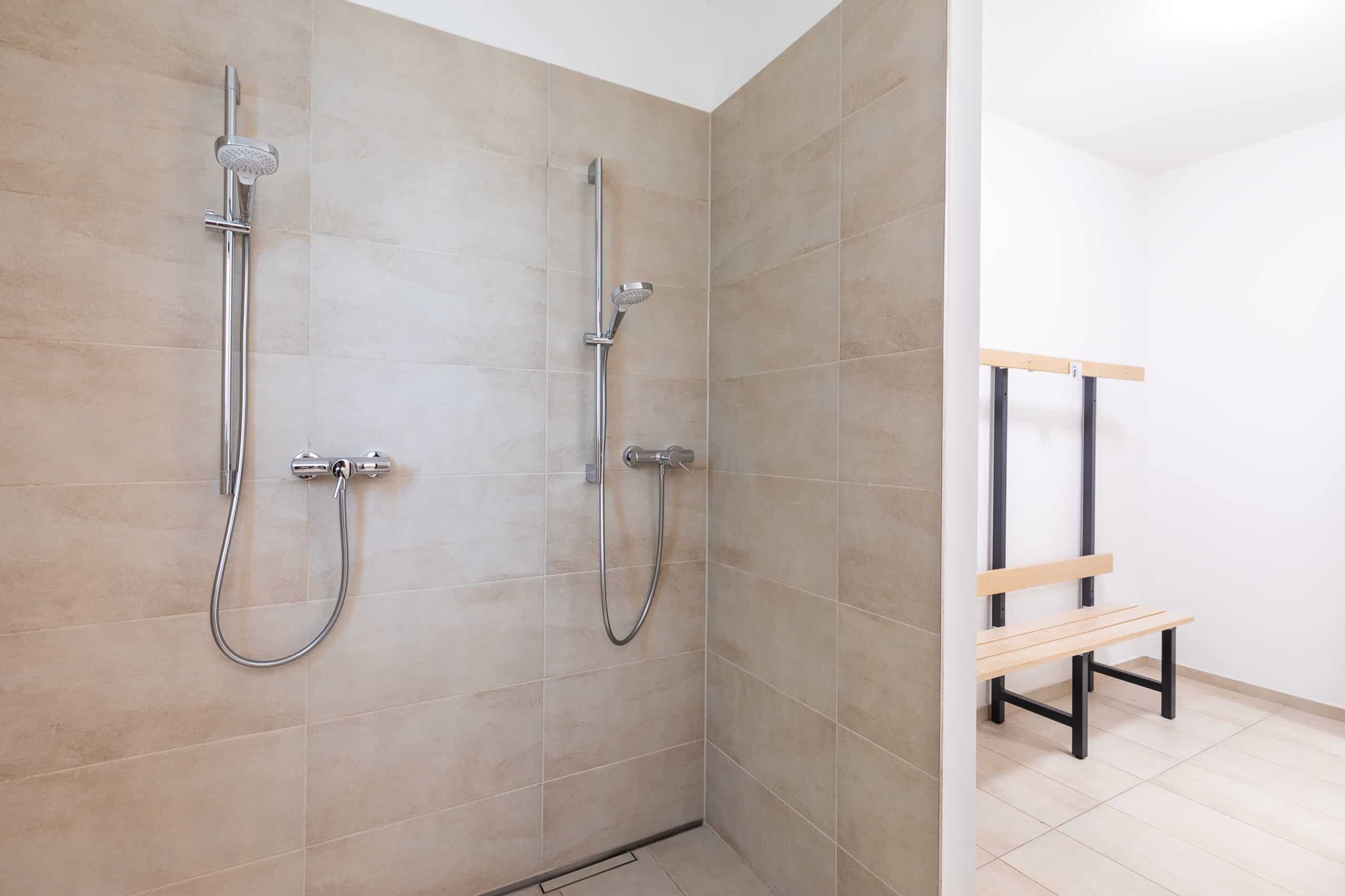 Bodengleiche Dusche mit Handbrause und Wandklappsitz in einem gefliesten Sanitärraum